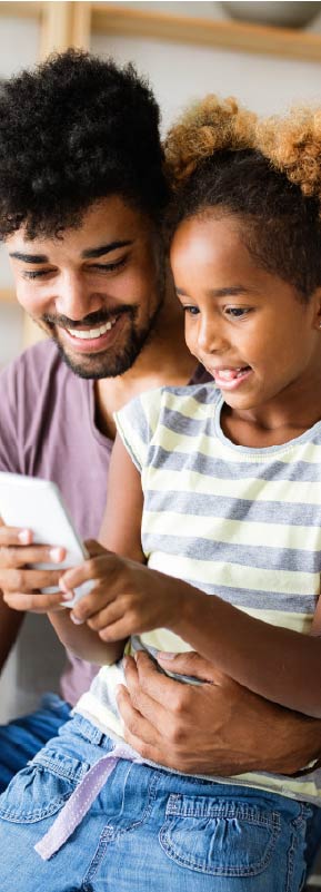 A father and daughter sitting together, smiling, and looking at a phone screen.