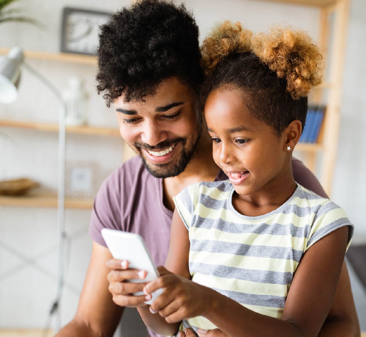 A father and daughter sitting together, smiling, and looking at a phone screen.