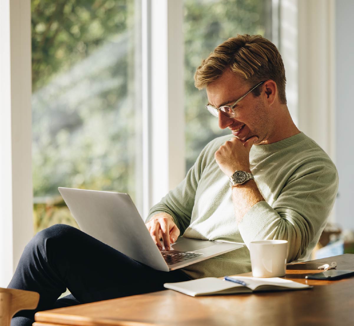 A happy man sitting at a table and working on a laptop