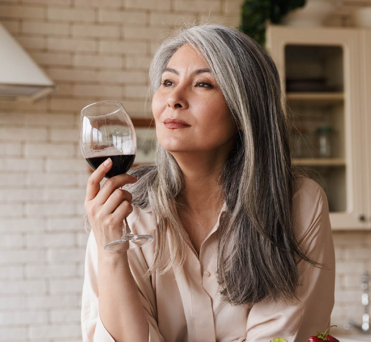 A retirement age woman holding a glass of red wine and gazing thoughtfully into the distance.