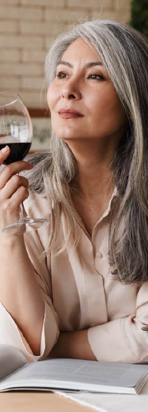 A retirement age woman holding a glass of red wine and gazing thoughtfully into the distance.