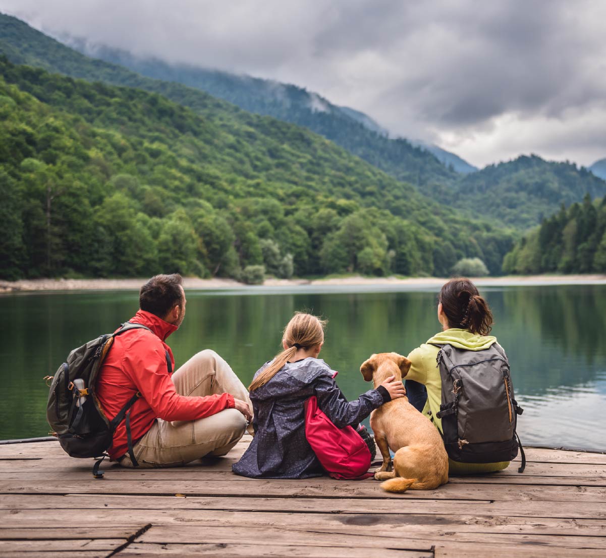 A family sitting on a dock, looking out at a lake.