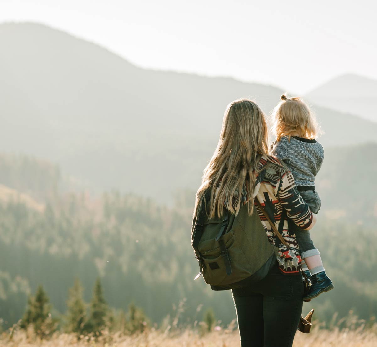 A mother holding her young daughter while they look out on a mountain vista.