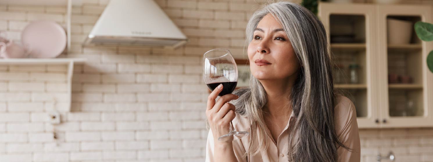 A retirement age woman holding a glass of red wine and gazing thoughtfully into the distance.