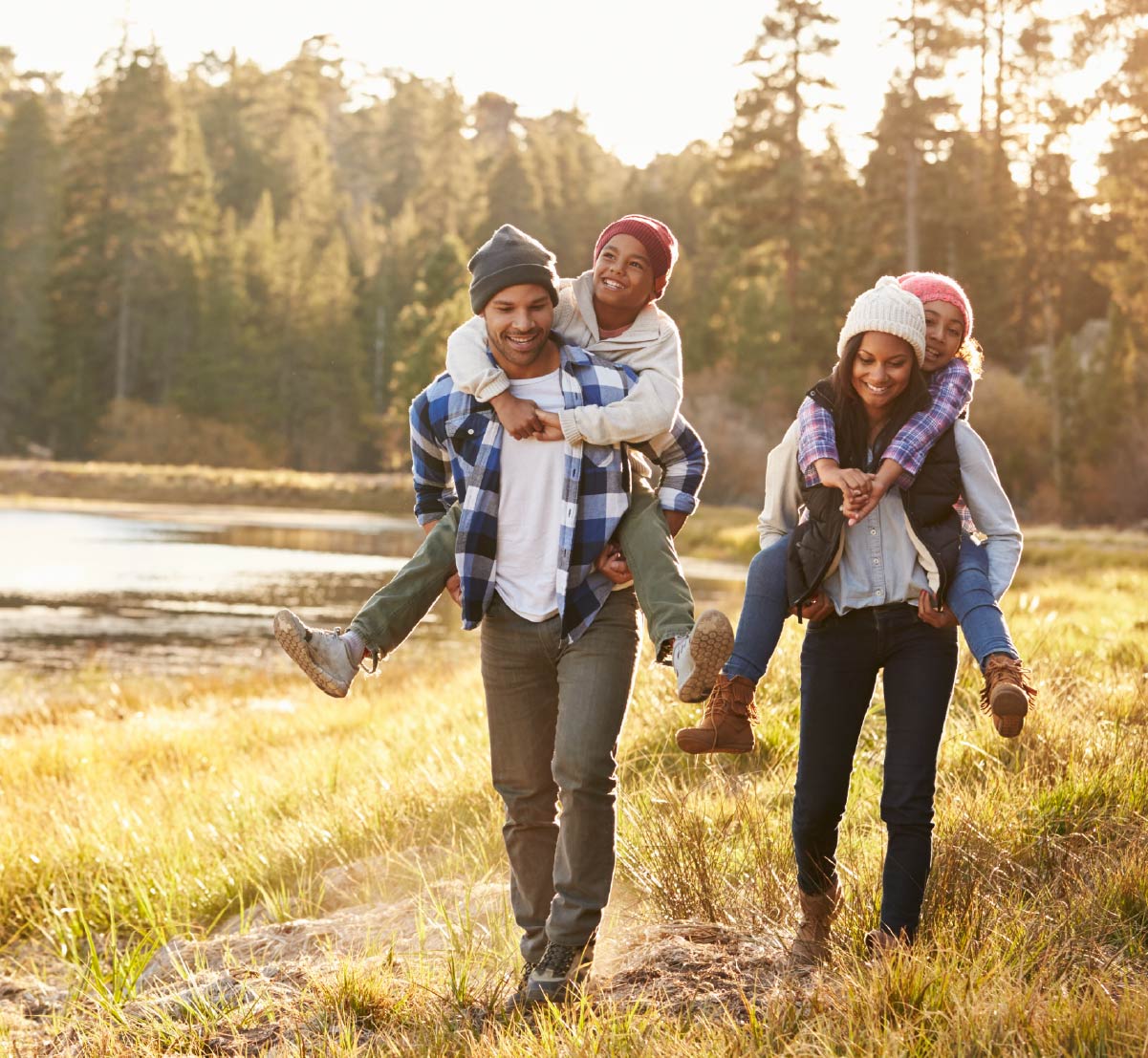 An attractive young couple giving their kids piggy back rides along the lake shore