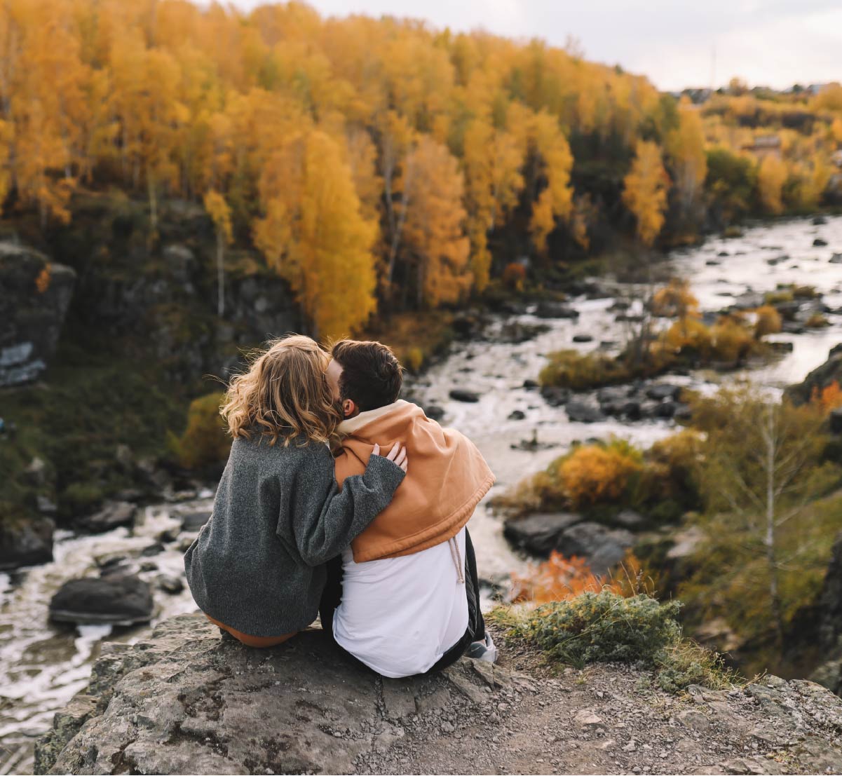 A couple sitting on a rock overlooking a river and forest