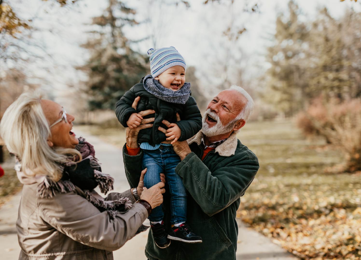 Grandparents playing with a young grandchild on a fall day.