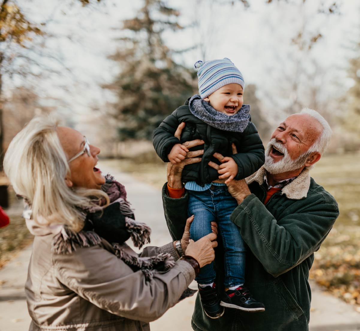 Grandparents playing with a young grandchild on a fall day.