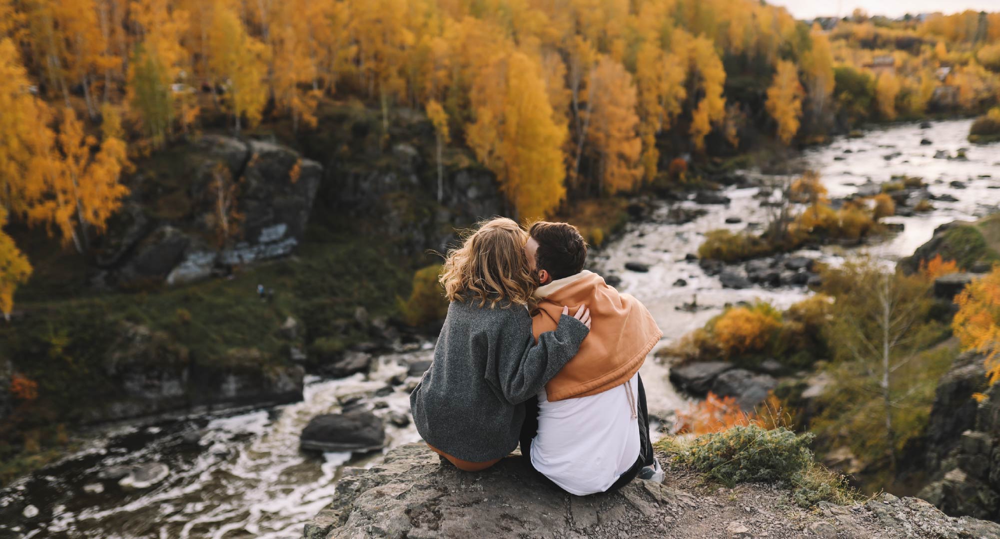 A couple sitting on a rock overlooking a river and forest