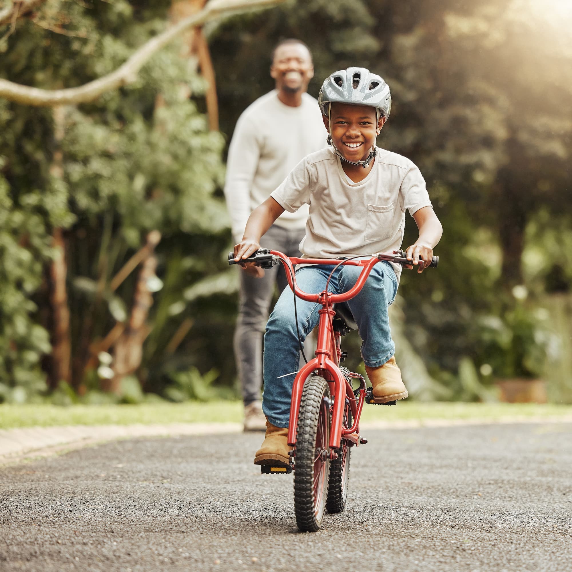 A young boy learning to ride a bike while his father smiles in the background